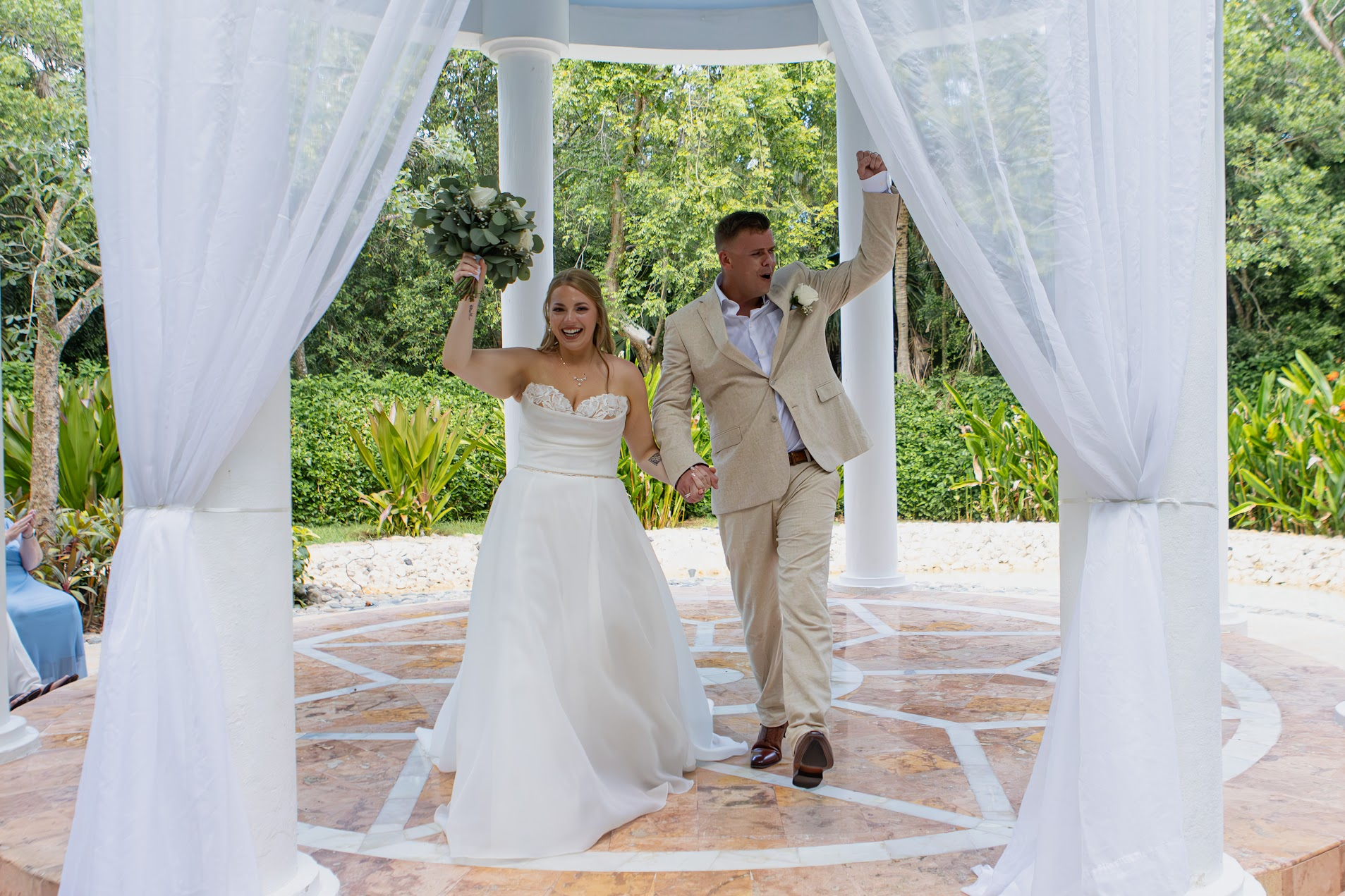 The newlyweds walking hand in hand beneath a white gazebo